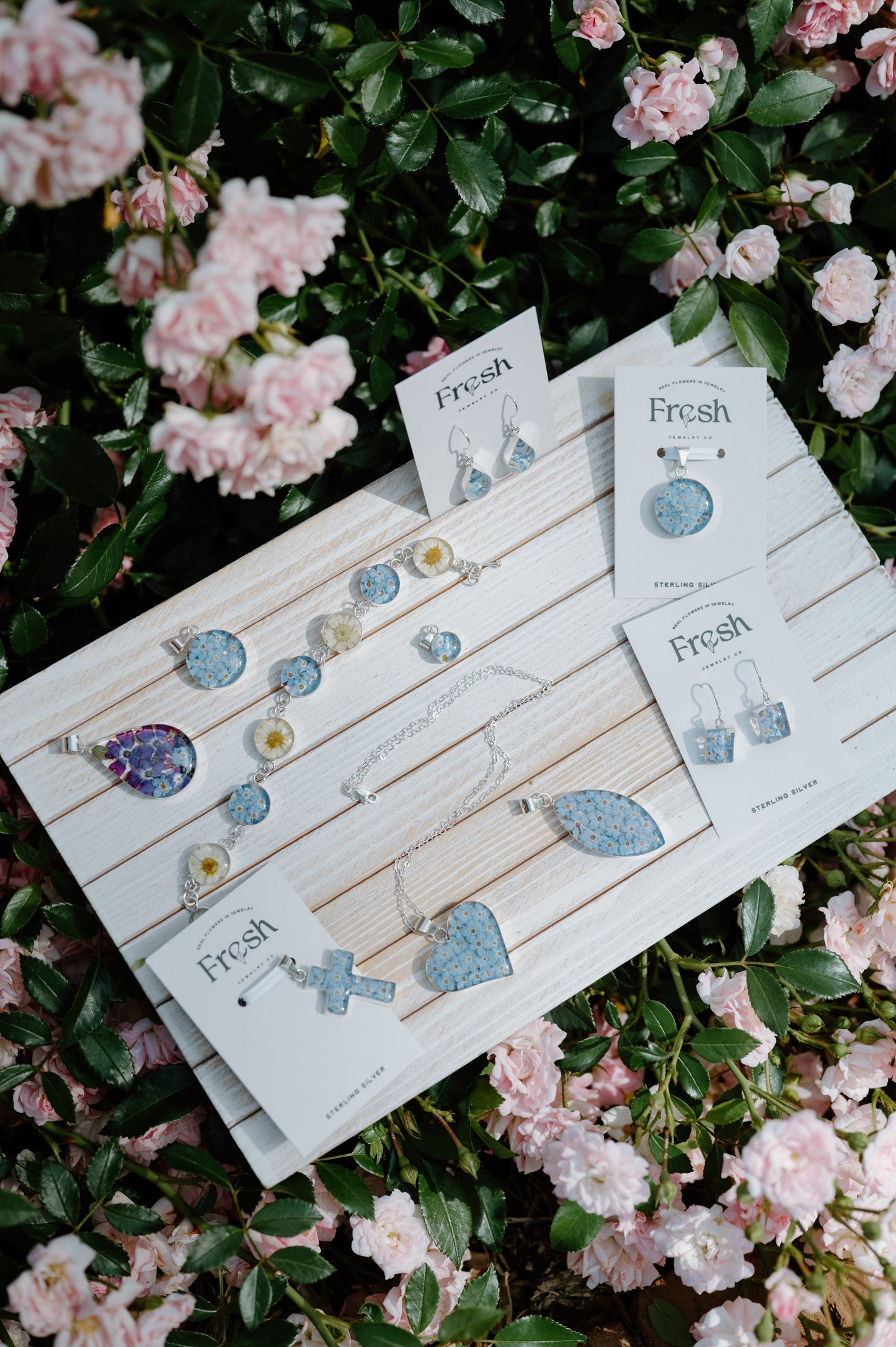 Jewelry set with 'Fresh' branding on a wooden display board, surrounded by pink flowers.