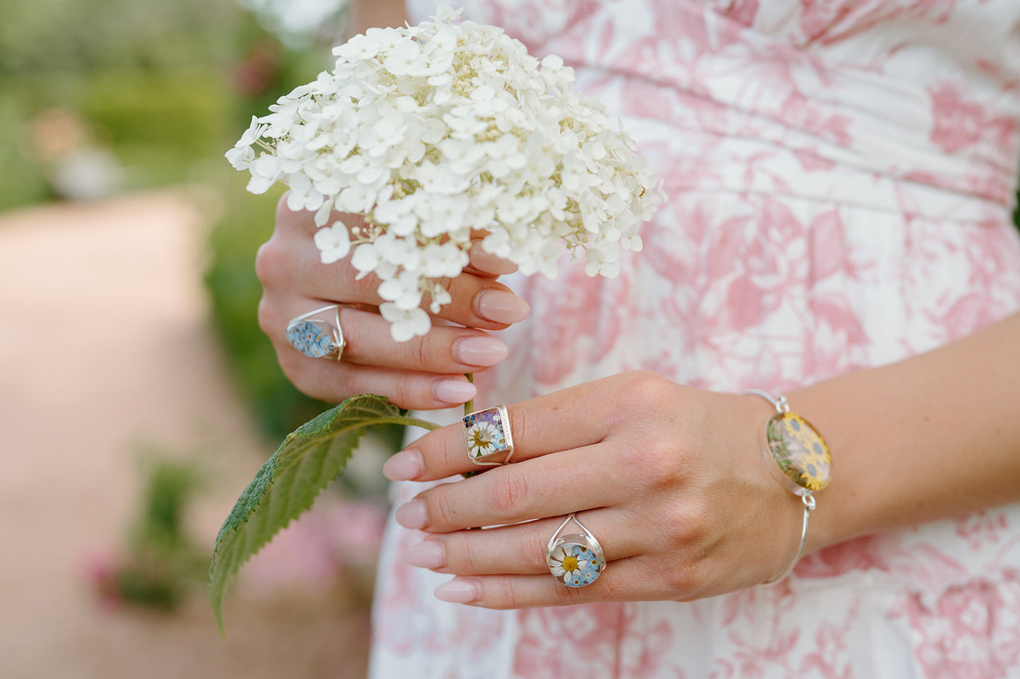 Close-up of hands holding white flowers with visible jewelry against a blurred natural background
