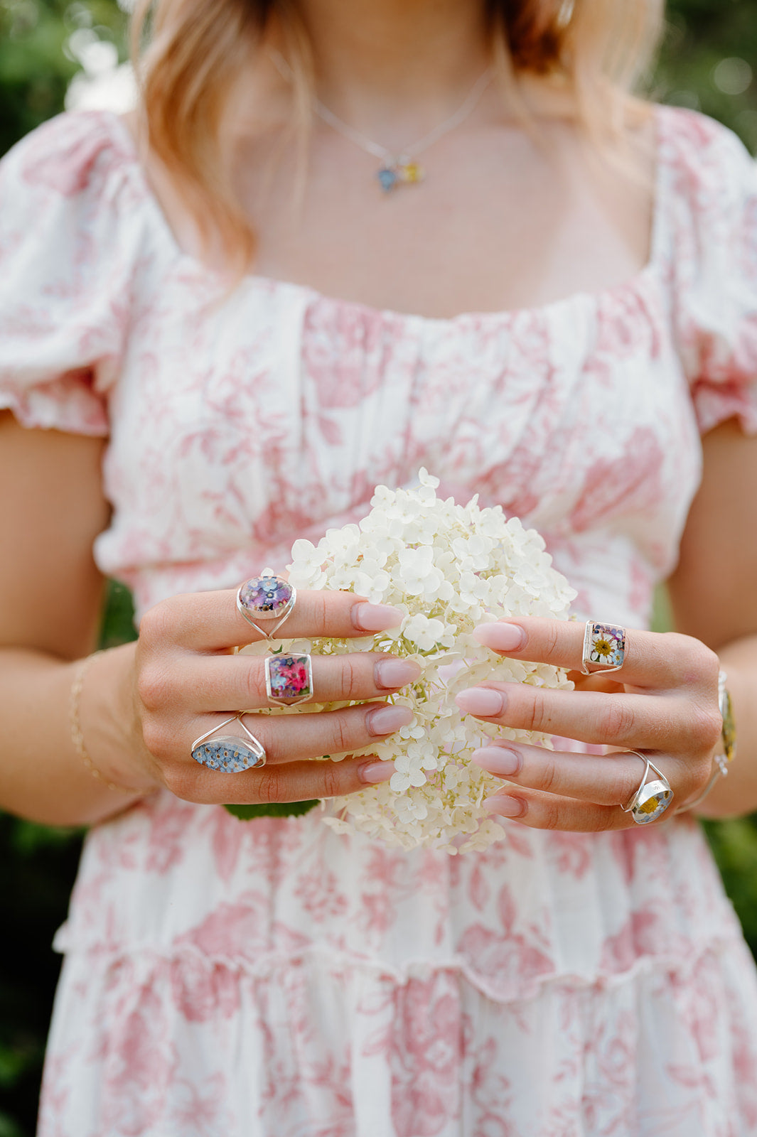 Person wearing multiple rings holding a bouquet of white flowers.