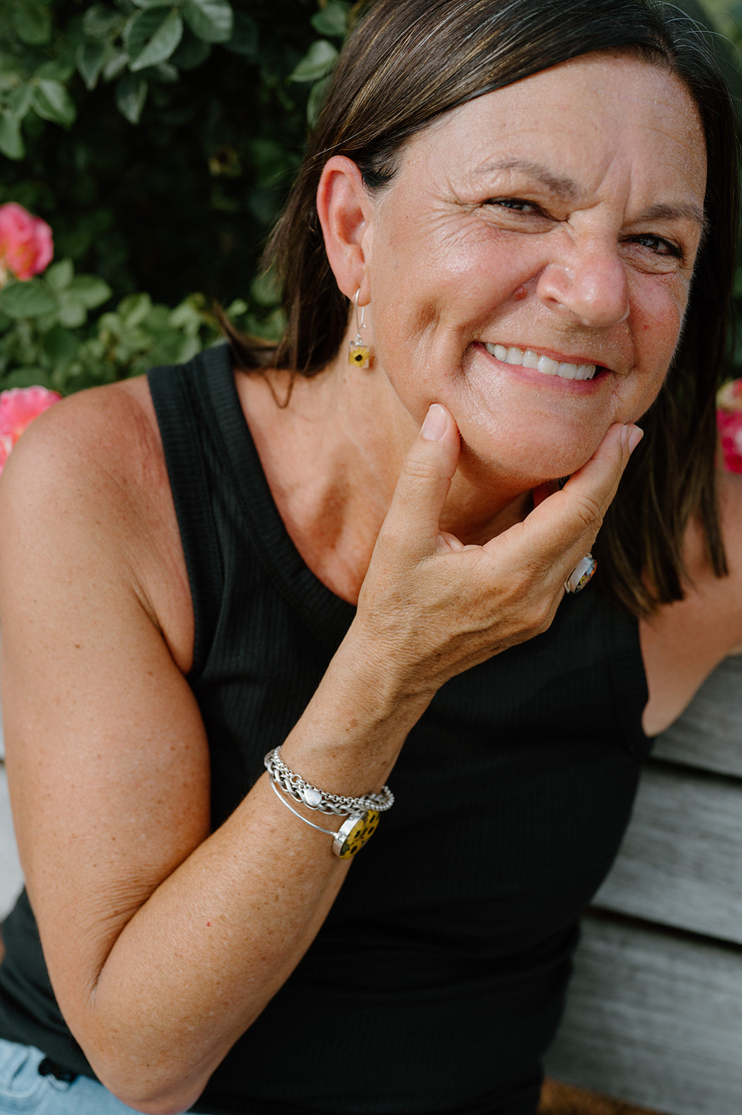 Woman with a smile, wearing a black sleeveless top and multiple bracelets, with a blurred background.