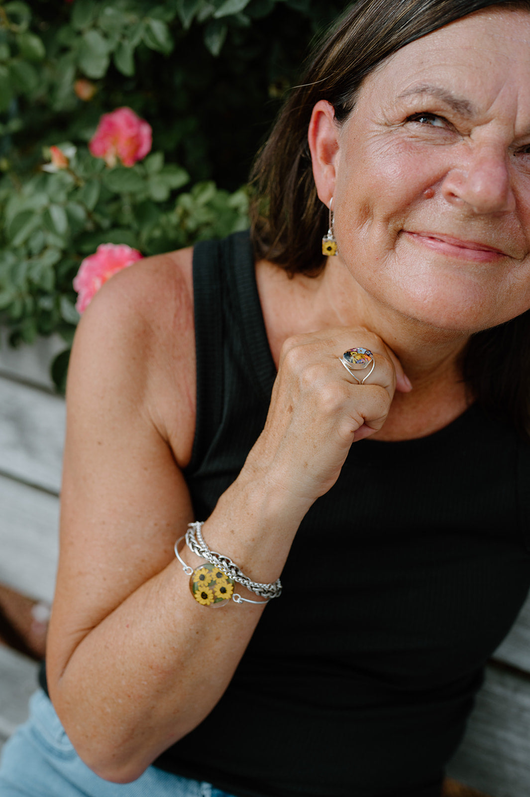 Woman wearing a black top and sunflower-themed jewelry outdoors with plants in the background