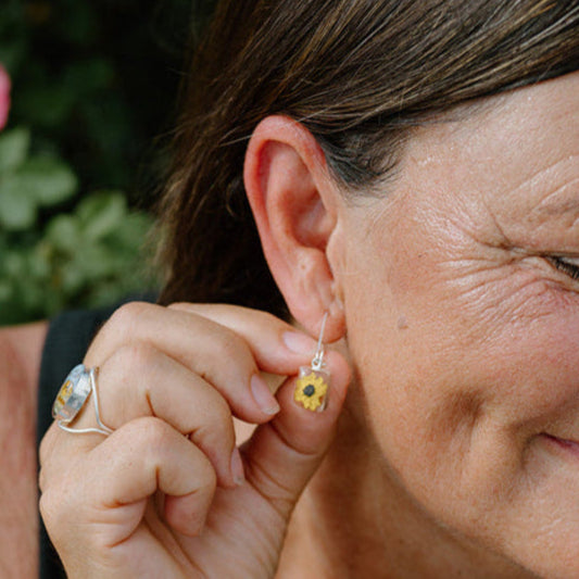 Woman wearing earrings and a bracelet, with flowers in the background