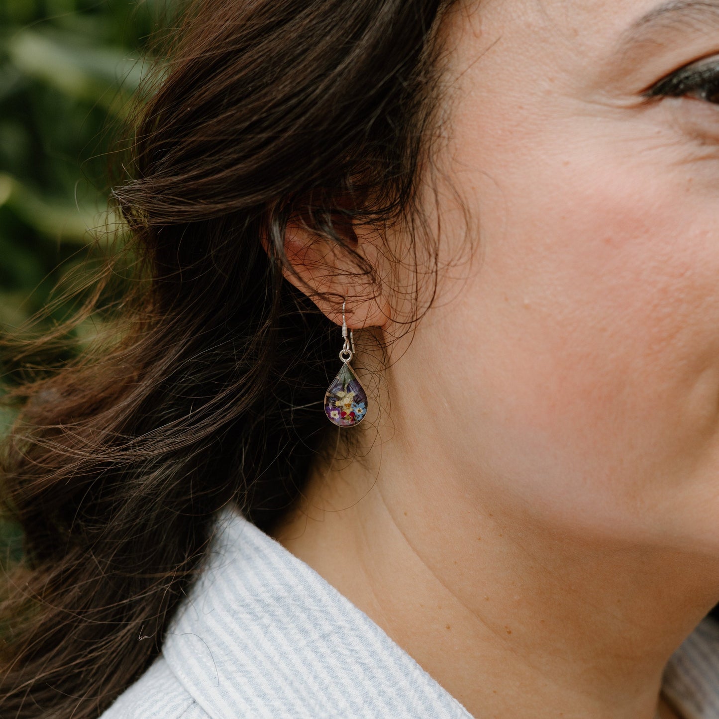 Close-up of a woman wearing earrings with a blurred green background