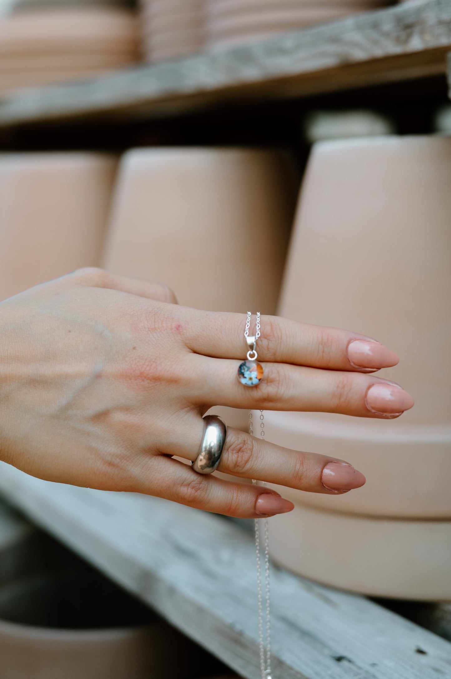Hand wearing two rings with a blurred background of ceramic pots