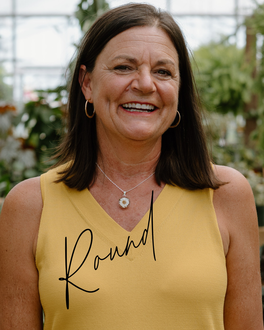 Woman wearing a yellow sleeveless top with 'Round' printed on it, standing in a greenhouse.