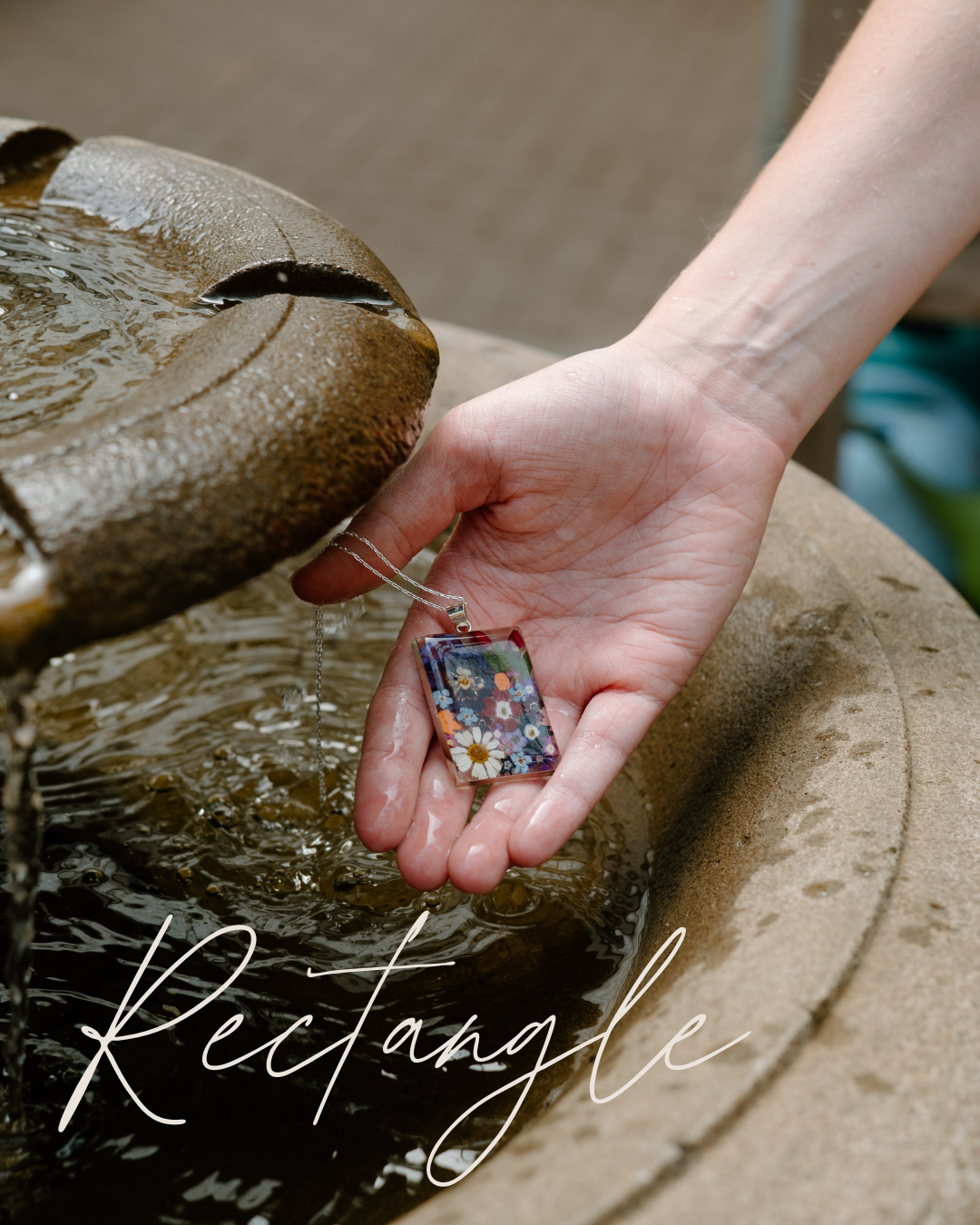 Hand holding a floral pendant near a water fountain with 'Rectangle' text overlay.