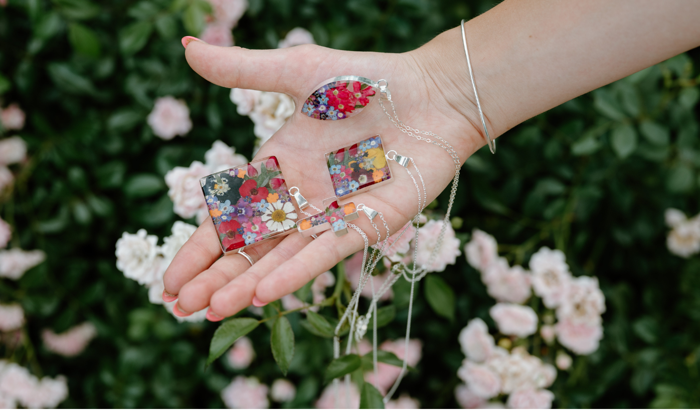 Hand holding colorful floral-patterned keychains with a blurred floral background