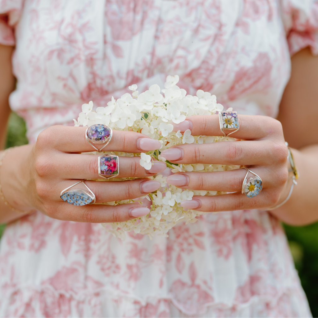 Close-up of hands wearing multiple rings with floral designs, holding a small bouquet of white flowers.