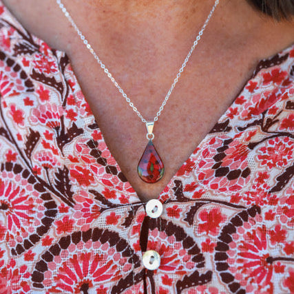 Necklace with a teardrop pendant worn by a person in a patterned shirt.