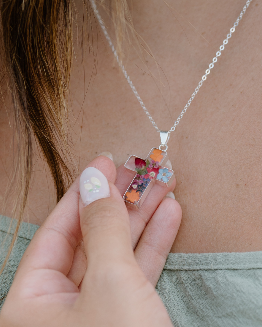 Necklace with a clear pendant featuring colorful stones held by a hand.