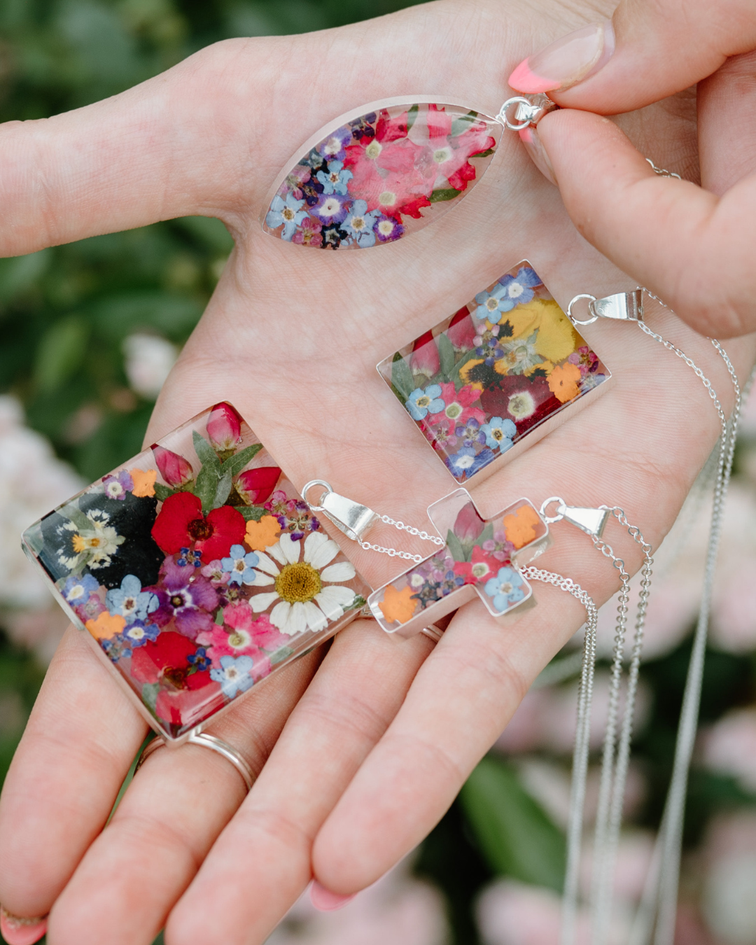 Hand holding floral resin necklaces with a blurred green background