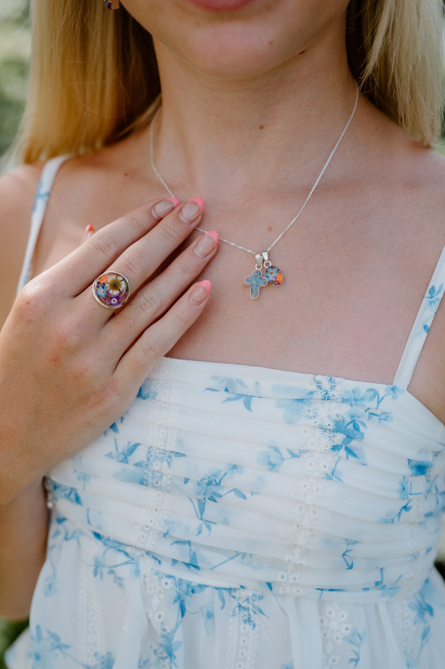 Woman wearing a white dress with blue floral patterns, a necklace with star-shaped pendants, and a ring.