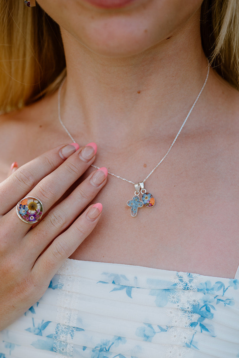 Woman wearing a white dress with blue floral patterns, holding a necklace with star-shaped pendants.