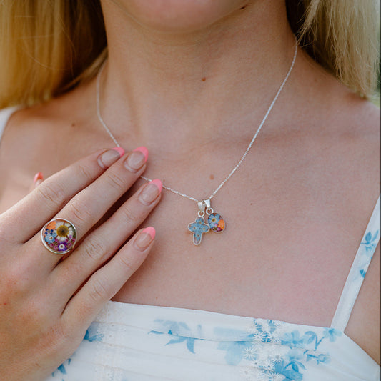 Woman wearing a white dress with blue floral patterns, a silver necklace with star-shaped pendants, and a colorful ring.