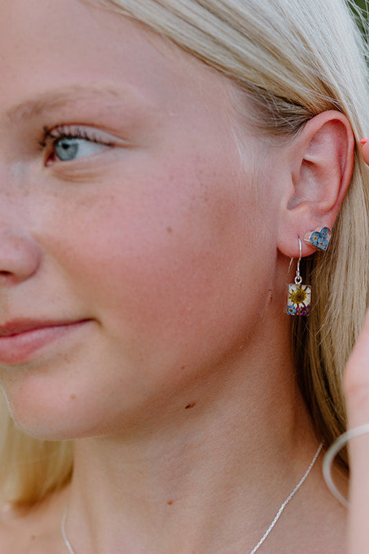 Woman adjusting earrings with a blurred outdoor background