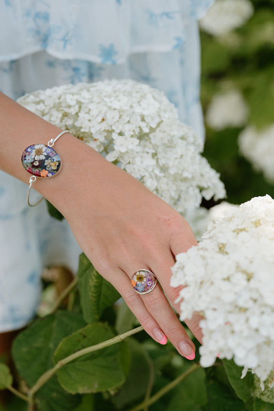 Person wearing a colorful bracelet and ring among white flowers