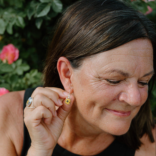 Woman wearing earrings and a bracelet, with flowers in the background