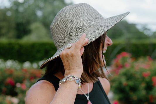 Woman wearing a wide-brimmed hat in a garden with flowers and greenery.