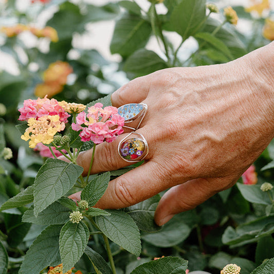 Hand with floral rings touching a plant with pink and yellow flowers