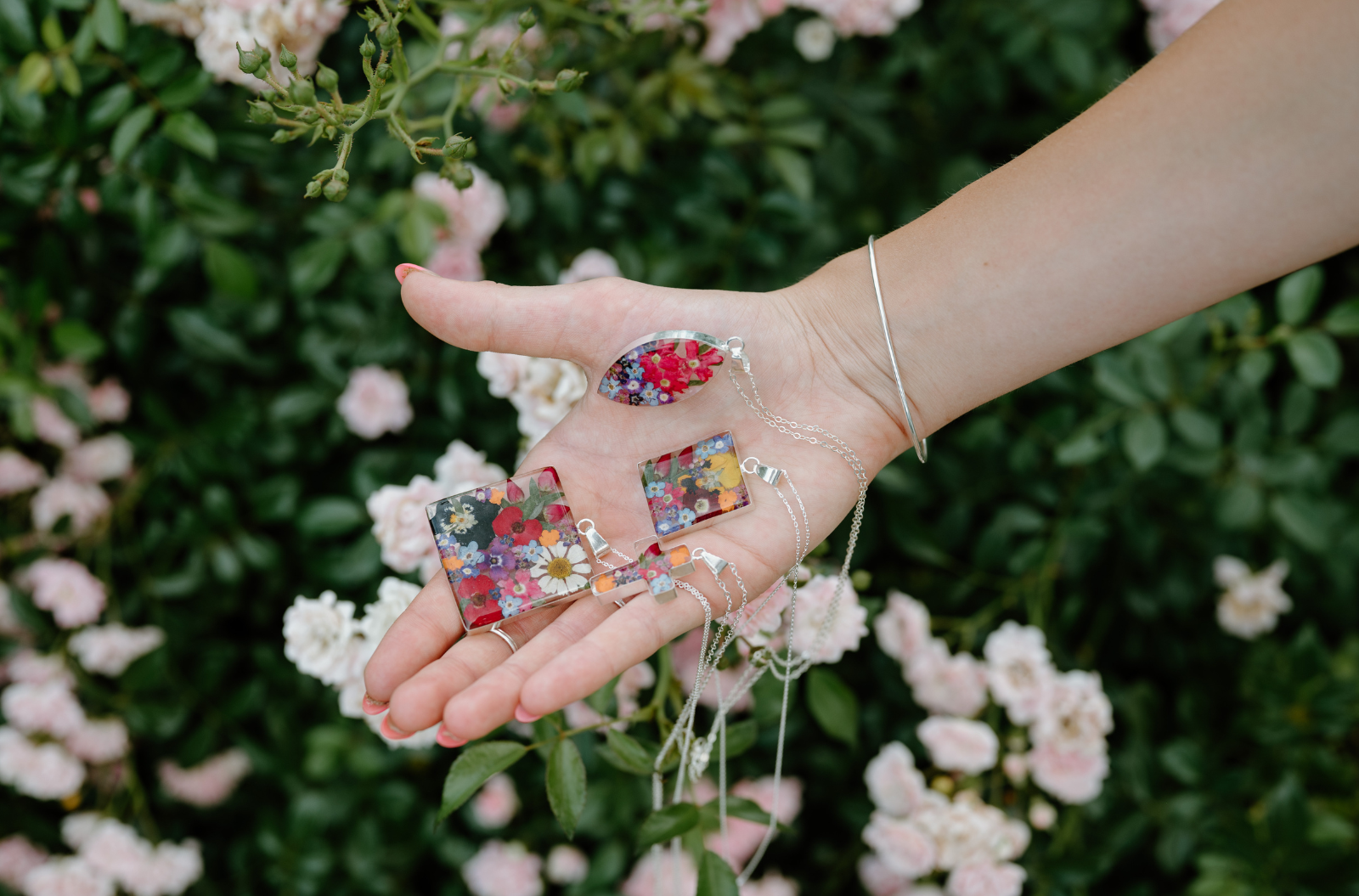 Hand holding colorful floral-patterned keychains with a blurred floral background