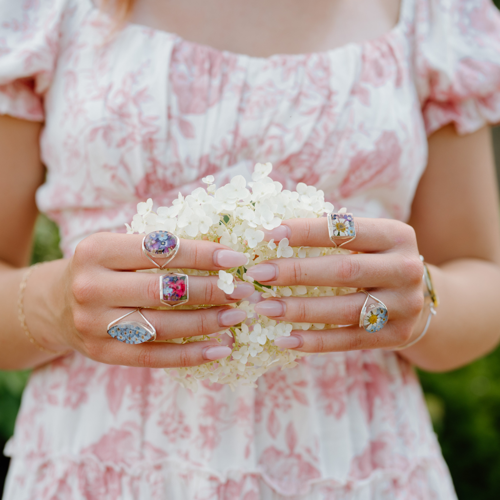 Person wearing multiple rings holding a small bouquet of flowers.